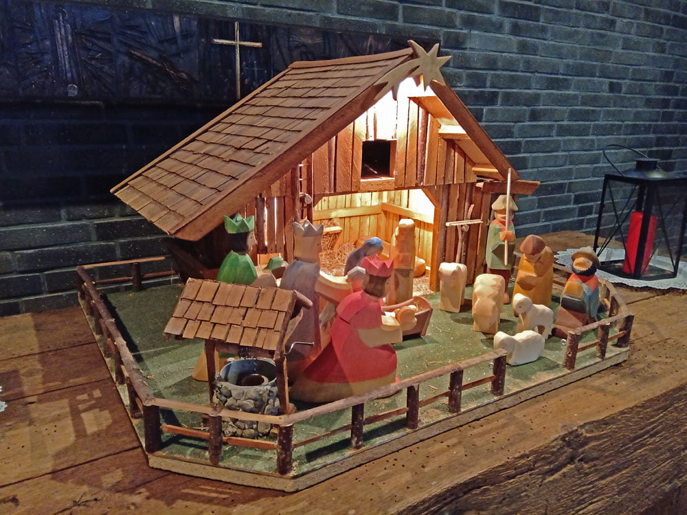 Ein kleiner aus Holz gebauter Stall mit einer Krippe und geschnitzen Figuren davor.